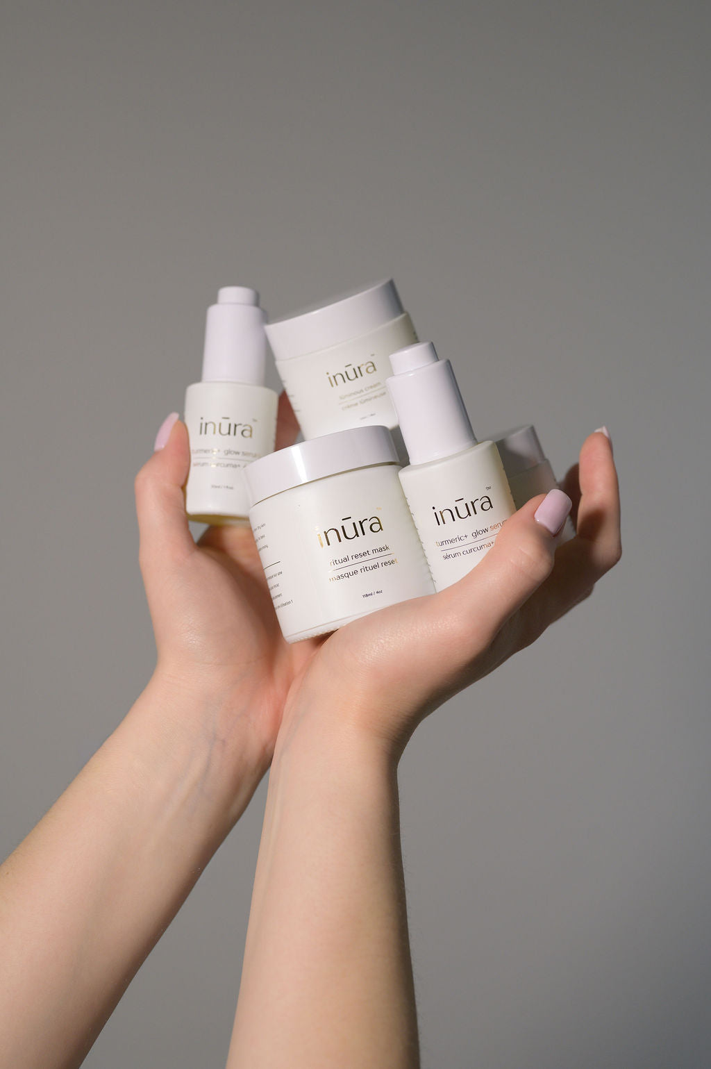 Four CertClean approved inūra skincare products held in hands, including turmeric+ glow serum, lūminous cream, nūrish cream, and ritual reset mask.